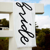 xo Fetti Bride Fringe Beach Towel with white fringe and black Bride logo, ideal for poolside photos.