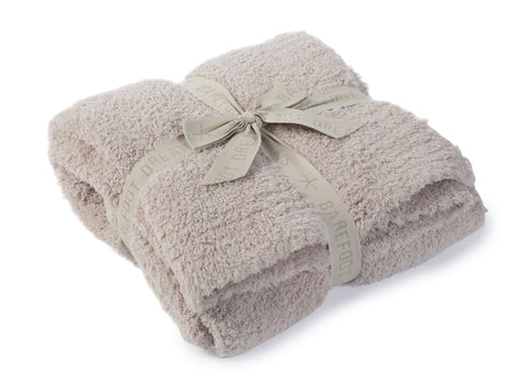 Barefoot Dreams CozyChic Throw Stone on bed beside pillows in a warm setting