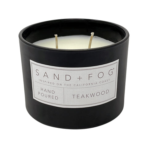 Sand + Fog teakwood candle on a table beside its decorative lid.