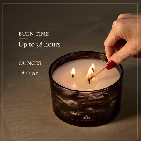Thymes Noir Woods candle burning close-up with evergreen and amber tones.
