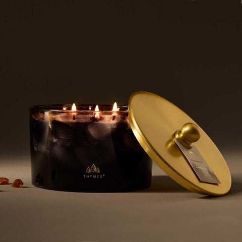 Thymes Noir Woods three-wick candle at dusk delivering a warm, inviting glow.