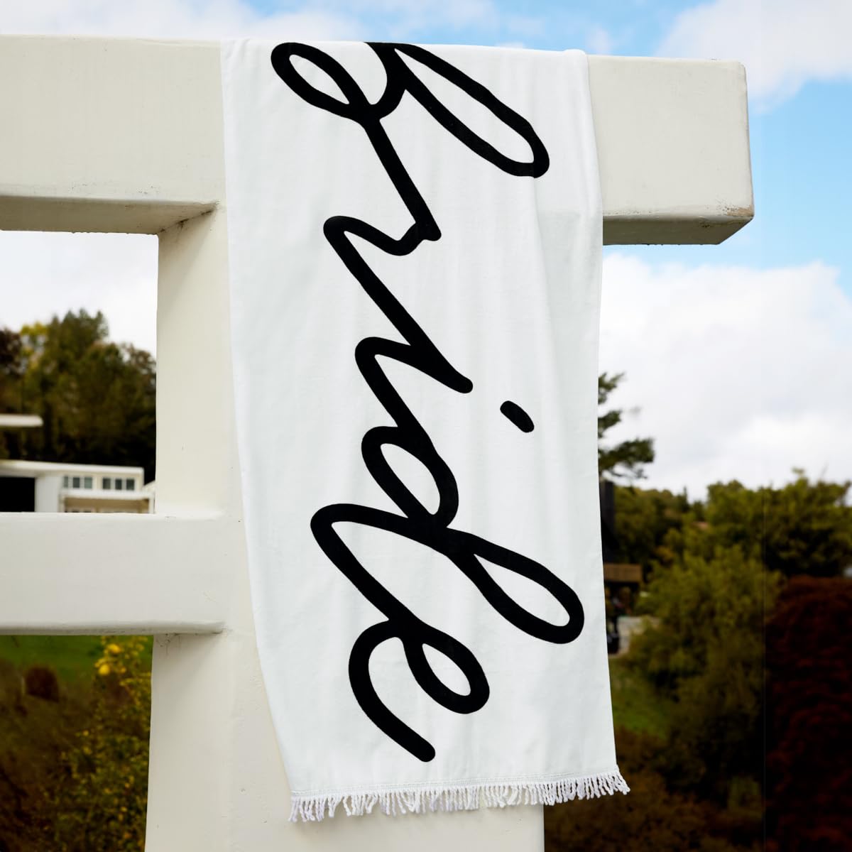 xo Fetti Bride Fringe Beach Towel with white fringe and black Bride logo, ideal for poolside photos.